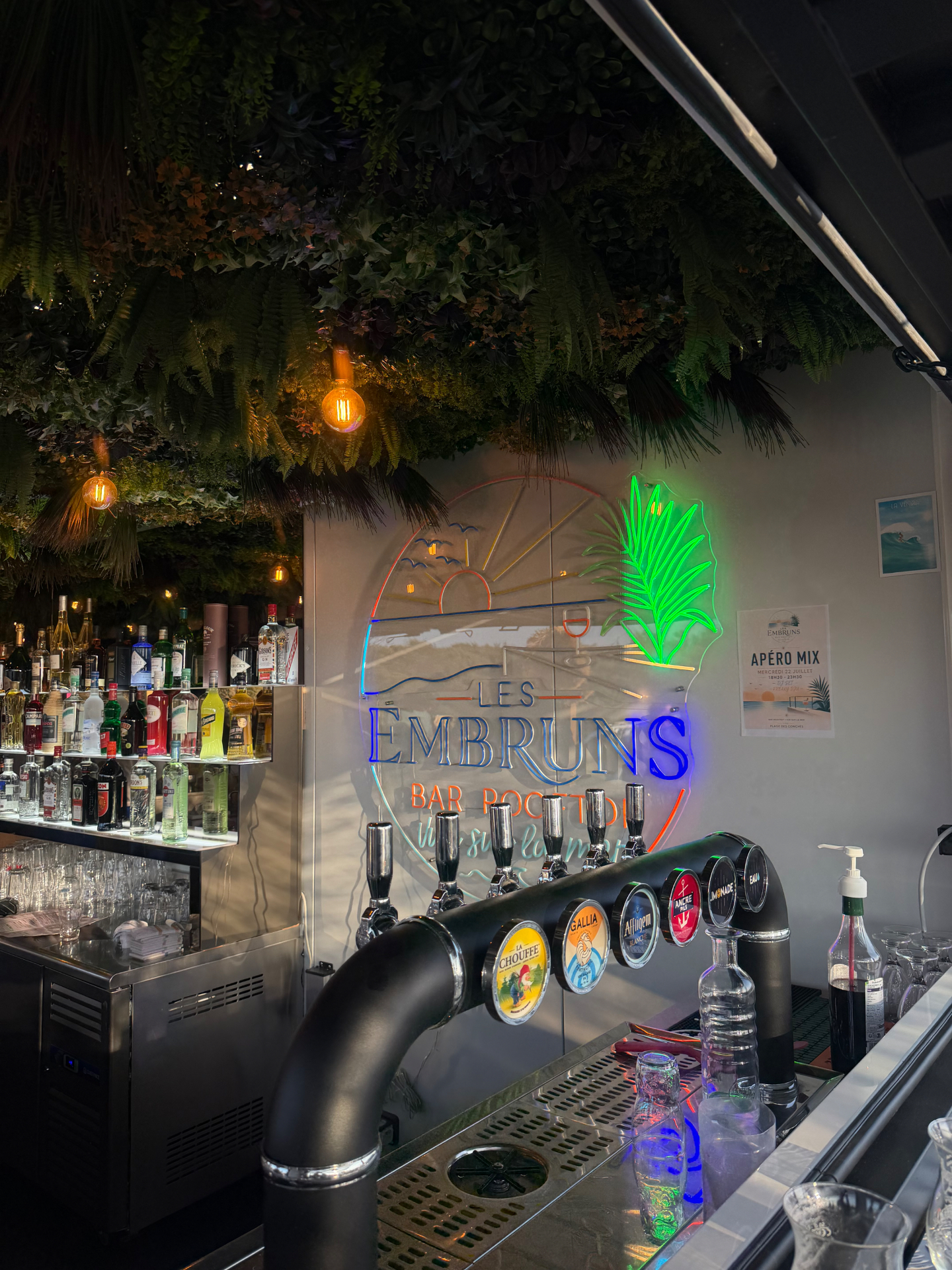 Bar des Embruns avec enseigne néon, tireuses à bière et plafond végétal